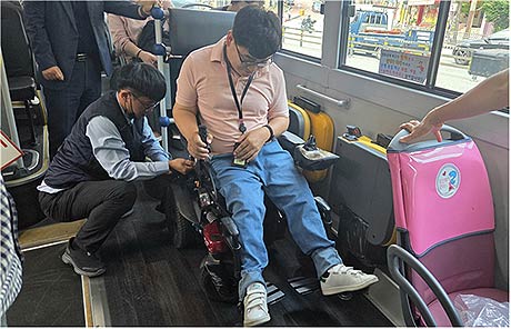 저상버스 운전기사가 휠체어에 좌석 고정벨트를 채우고 있는 장면