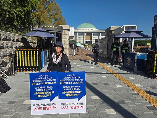 국정감사가 진행 중인 국회 정문 앞에서 한 지역아동센터 관계자가 인건비 가이드라인 100 적용을 촉구하는 피켓을 들고 1인 시위를 벌이고 있다